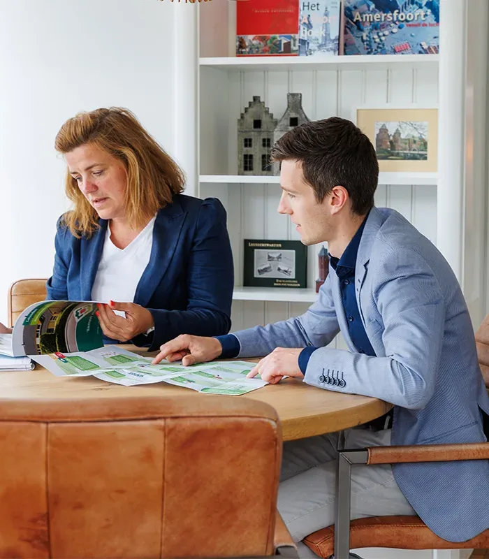 Woonadviesgesprek bij Ditters Makelaars Amersfoort – persoonlijk en deskundig Makelaar van Ditters Amersfoort voert een persoonlijk woonadviesgesprek met een klant aan tafel, bespreekt verkoop- en aankoopmogelijkheden met woningbrochure.